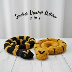 May include: Two crocheted snake toys. One is black and yellow striped, the other is solid yellow with black markings. The snakes have embroidered eyes and are coiled. The text "Snakes Crochet Pattern 2 in 1" is above the snakes.