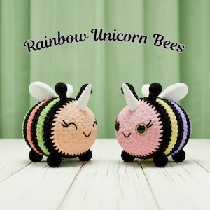 May include: Two crocheted bee-shaped toys with rainbow stripes and white wings. One is peach-colored, the other pink. Both have black antennae, smiling faces, and white unicorn horns. The text "Rainbow Unicorn Bees" is above them.