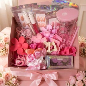 May include: A pink gift box filled with beauty accessories including a clear tumbler with a pink lid and straw, various pink hair clips, satin scrunchies, hair ties, lip gloss tubes, false eyelashes in a glittery box, and holographic pouches.