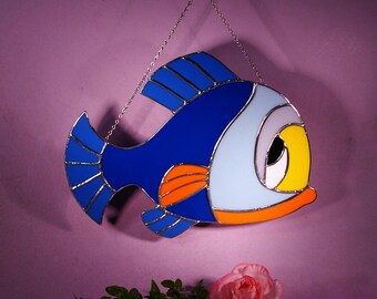 May include: A stained glass fish with blue, orange, and yellow accents. The fish is hanging from a silver chain.