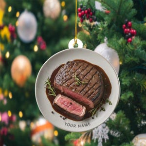May include: A round, ceramic Christmas ornament featuring a grilled steak on a plate with sauce and rosemary. The steak is cut to show the inside. The text "YOUR NAME" is printed on the plate.