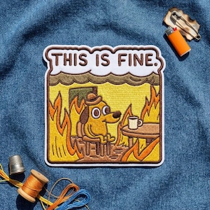 May include: A rectangular embroidered patch featuring a cartoon dog wearing a hat, sitting at a table with a coffee mug amidst flames. The text THIS IS FINE. is stitched in brown letters on a white background at the top of the patch.