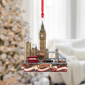 May include: A London-themed Christmas ornament featuring Big Ben, a red double-decker bus, and Tower Bridge. The ornament has a red ribbon for hanging and a banner that reads "LONDON". The ornament is a festive souvenir.