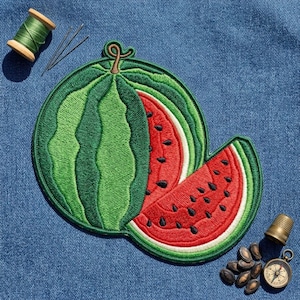 May include: An embroidered watermelon patch featuring a whole green melon with a red slice showing black seeds. The patch is surrounded by a green thread spool, three sewing needles, a metal thimble, and a small round brass compass.