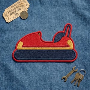 May include: An embroidered patch shaped like a red bumper car with a dark blue base, yellow accents, and a dark blue seat. The patch is displayed alongside a vintage amusement park ticket labeled Bumper Cars and a set of metal keys on a ring.