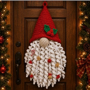 May include: A crocheted gnome wall hanging featuring a tall red hat adorned with green holly leaves and red berries. The gnome has a beige nose and a long, white, curly beard decorated with small ornaments including stars, a candy cane, and bells.