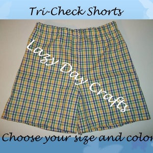 May include: Yellow, green, and purple plaid shorts with a white elastic waistband. The shorts have the text "Lazy Day Crafts" printed on them. Tri-Check Shorts.
