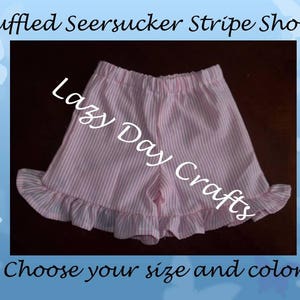 May include: Pink and white striped seersucker shorts with a ruffled hem. The shorts are made by Lazy Day Crafts.