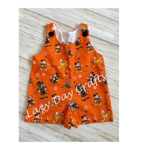 May include: Orange overalls with a Halloween Mickey Mouse print. The overalls have black buttons and straps. The text "Lazy Day Crafts" is visible on the front of the overalls.