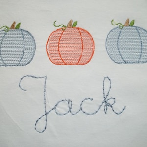 May include: A white embroidered baby onesie with three pumpkins, two blue and one orange, and the name "Jack" embroidered below.