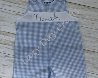May include: A blue and white gingham baby overall with a white band across the chest that says "Noah" in white embroidery.
