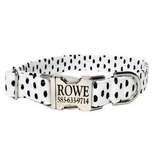 May include: A white pet collar featuring a black dalmatian-style spot pattern. The collar includes a silver-toned metal side-release buckle engraved with the name ROWE and the phone number 583-633-9714, along with a matching silver metal D-ring.