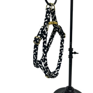 Peut inclure: Harnais r&eacute;glable noir et blanc &agrave; imprim&eacute; os de chien avec des ferrures dor&eacute;es. Le harnais est suspendu &agrave; un pr&eacute;sentoir en m&eacute;tal noir.