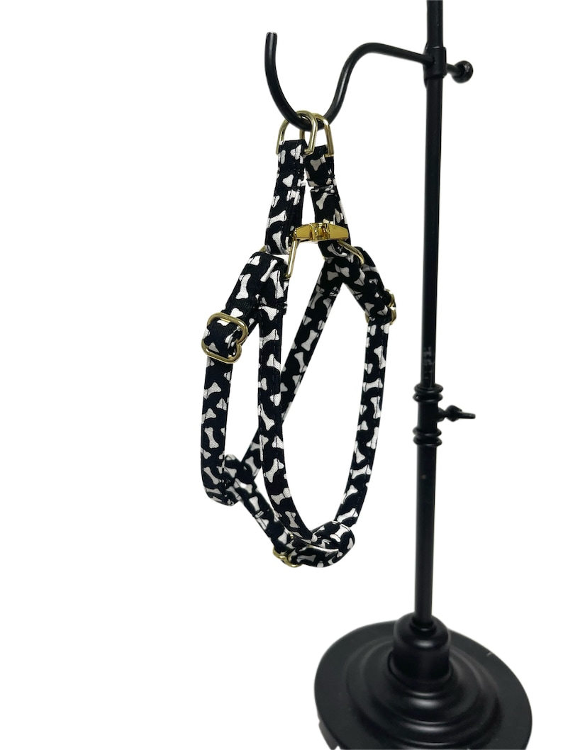 Peut inclure: Harnais r&eacute;glable noir et blanc &agrave; imprim&eacute; os de chien avec des ferrures dor&eacute;es. Le harnais est suspendu &agrave; un pr&eacute;sentoir en m&eacute;tal noir.