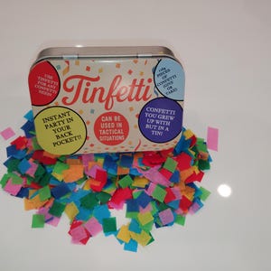 Könnte beinhalten: Eine dekorative "Tinfetti"-Dose mit bunten Konfetti. Auf der Dose steht "Sofortige Party in Ihrer Hosentasche!!" und "Konfetti, mit dem Sie aufgewachsen sind, aber in einer Dose!" Das Konfetti ist in verschiedenen Farben.