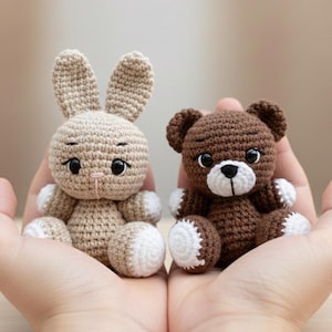 Op de afbeelding: Twee handgemaakte gehaakte knuffels: een beige konijn met witte accenten en een bruine teddybeer met witte accenten. Beide hebben zwarte ogen en zitten rechtop. Het konijn heeft lange oren en een roze neus.