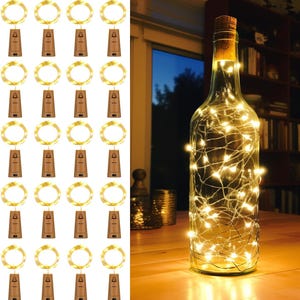 Op de afbeelding: Een heldere glazen fles met een kurk, gevuld met kleine, warmwitte LED-lampjes. Links worden meerdere sets kurklampjes met een cirkelvormige lichtketting weergegeven. De lampjes staan op een houten tafel.