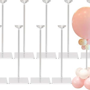 Puede incluir: Soportes de globos de acrílico transparente con bases cuadradas. Los soportes tienen un diseño alto y delgado con una pequeña parte superior redonda para sostener globos. Un soporte sostiene un gran globo rosa con globos más pequeños.