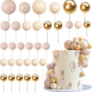 May include: A collection of cake toppers in various colors, including gold, cream, and blush pink. The toppers are spherical and attached to thin, green stems. A decorated cake with matching sphere accents is also shown.