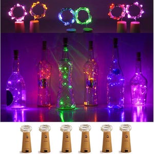 Puede incluir: Una colección de luces decorativas para botellas con corchos. La imagen muestra varias botellas de vidrio iluminadas con luces de cadena LED de colores. Los corchos tienen pequeñas luces en la parte superior. Las luces son de varios colores, incluyendo morado, verde y naranja.