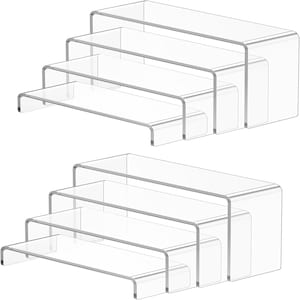 May include: Clear acrylic display risers, a set of four arranged in a stepped configuration. The rectangular risers have rounded edges, designed for product display. The transparent design offers a clean, modern presentation. Each riser is measured in centimeters.