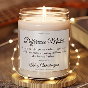May include: A lit soy wax candle in a clear glass jar with a white label. The label reads: Zen Flow Designs, Difference Maker, A truly special person whose generosity and heart make a lasting difference in the lives of others. Also known as: Kerry Washington, Eco-Friendly Soy Wax Candle.