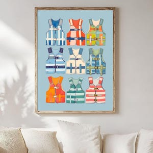 May include: A framed print featuring nine colorful life vests against a light blue background. The vests are in various colors, including blue, orange, green, and red, with white stripes and buckles. The artwork is displayed in a living room setting.