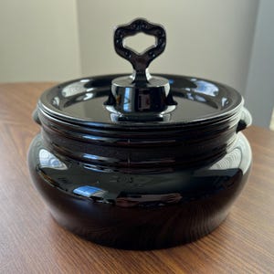 Peut inclure: Un plat de service en céramique noire brillante avec un couvercle et une poignée. Le plat a un corps arrondi avec une bande texturée au milieu et de petites poignées sur les côtés. Le couvercle comporte une poignée décorative.