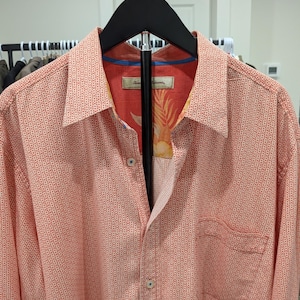 May include: Coral-colored button-down shirt with a small dot pattern. The shirt has a chest pocket and a patterned interior lining. The shirt is hanging on a black hanger.