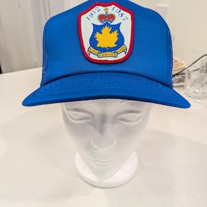 Könnte beinhalten: Blaue Trucker-Mütze mit Mesh-Rückseite und gebogenem Schirm. Auf der Vorderseite befindet sich ein Wappen mit dem Text "King Edward School" und den Jahreszahlen "1912" und "1987". Das Wappen zeigt ein gelbes Ahornblatt und eine Krone.