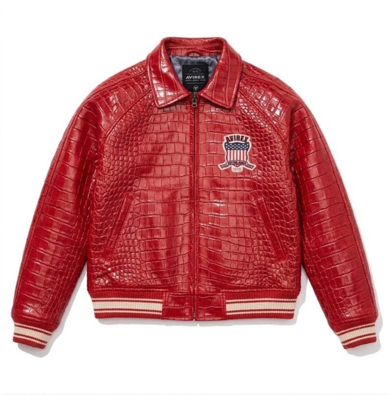 May include: A red leather jacket with a crocodile texture. The jacket features a collared neckline, a zip closure, and a chest patch with the text "AVIREX". The cuffs and hem have a striped design.