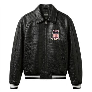 Puede incluir: Chaqueta de cuero negro con textura de cocodrilo. La chaqueta tiene cuello, cierre de cremallera y un parche en el pecho con el texto "AVIREX". Los pu&ntilde;os y el dobladillo tienen detalles a rayas blancas y negras.