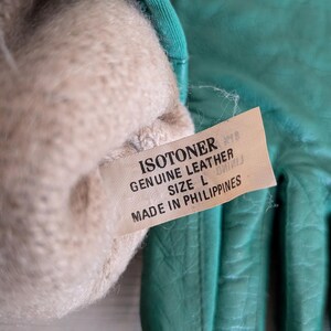 May include: A pair of teal Isotoner leather gloves, size L, with a soft, beige lining. The gloves are made in the Philippines. The tag reads "Genuine Leather".