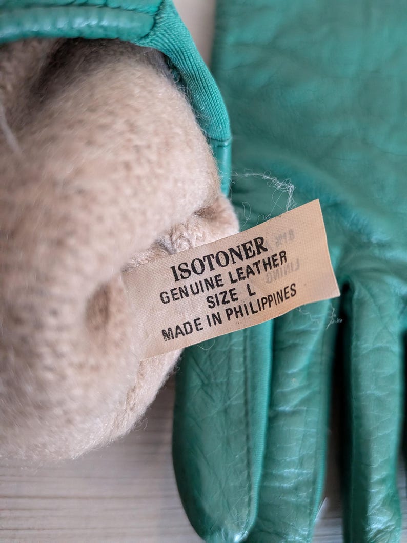May include: A pair of teal Isotoner leather gloves, size L, with a soft, beige lining. The gloves are made in the Philippines. The tag reads "Genuine Leather".
