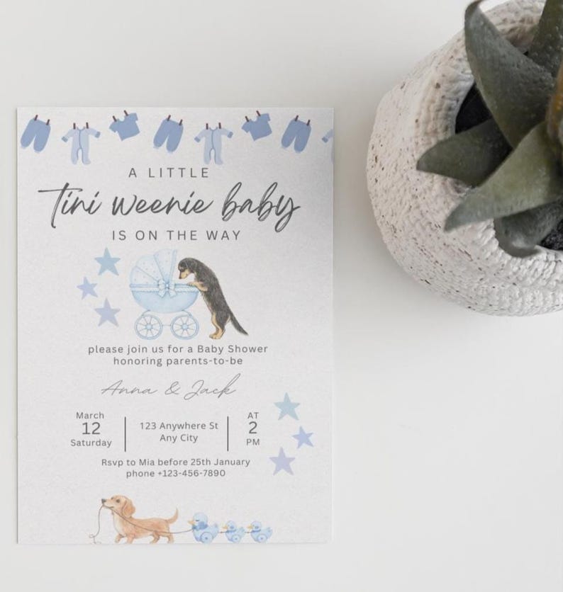 May include: A white baby shower invitation card featuring blue baby clothes, stars, and two dachshund dogs. The text reads: A LITTLE Tini Weenie baby IS ON THE WAY, please join us for a baby shower honoring parents-to-be, Anna & Jack, March 12, 123 Anywhere St, 2 PM.