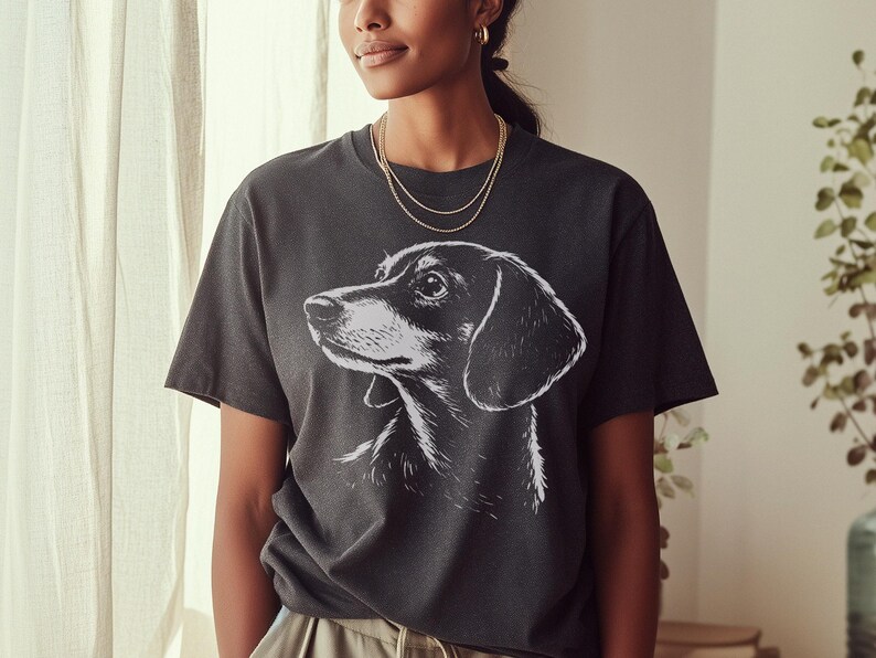 May include: Dark gray t-shirt featuring a black and white illustration of a dachshund dog. The dog's profile is visible, with detailed shading. The shirt has a classic crew neck and short sleeves, suitable for casual wear.