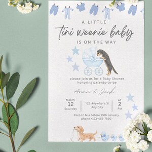 May include: A white baby shower invitation card featuring blue baby clothes, a blue carriage with a dachshund, and a light brown dachshund pulling blue toy ducks. Text reads: A LITTLE Tini weenie baby IS ON THE WAY, Anna & Jack, March 12.