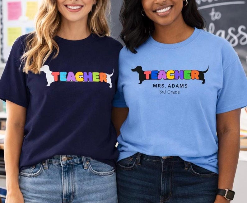 Pode incluir: Duas mulheres vestindo camisetas combinando. Uma camisa &eacute; azul marinho, a outra azul claro. Ambas as camisas t&ecirc;m a palavra "TEACHER" em letras coloridas com um gr&aacute;fico de cachorro dachshund. A camisa azul marinho tem um cachorro branco, a camisa azul claro tem um cachorro preto.