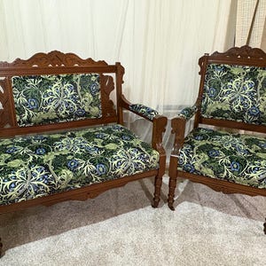 May include: A set of antique wooden furniture, including a loveseat and an armchair. The frames are a dark brown color, and the cushions are upholstered with a green, blue, and white floral pattern. The furniture has ornate carvings.