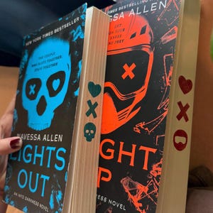 May include: Two books by Navessa Allen are displayed. The first book, "Lights Out," has a blue skull graphic and the text "The Couple Who Slays Together, Stays Together." The second book, "Nightfall," has an orange graphic and the text "Get on Your Knees and Prey."