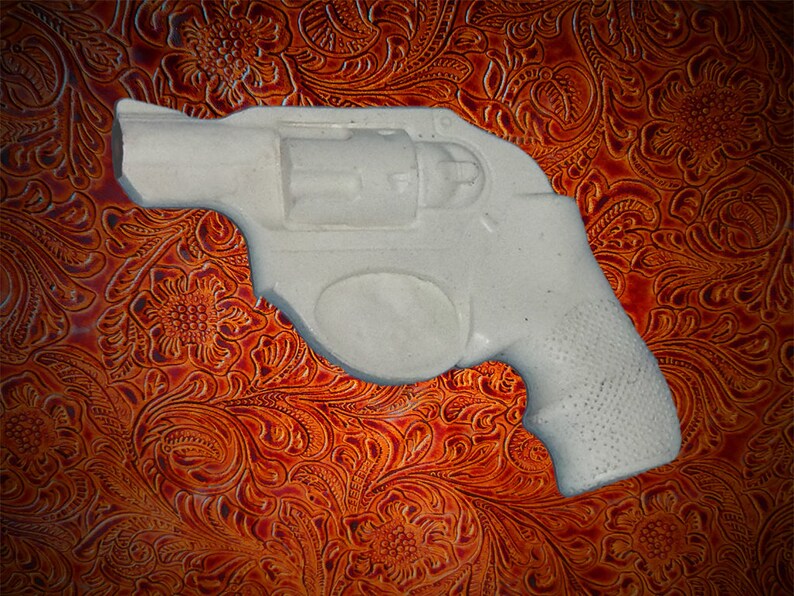 May include: A white plastic replica of a revolver handgun on a brown patterned background.