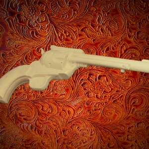 May include: A wooden toy gun, resembling a revolver, with a light brown finish. The gun is lying on a brown patterned surface.