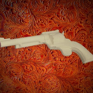 May include: A white plastic toy gun shaped like a revolver. The gun is lying on a brown leather background with a floral pattern.