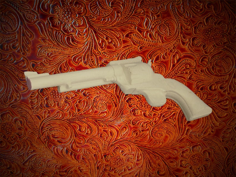 May include: A white plastic toy gun shaped like a revolver. The gun is lying on a brown leather background with a floral pattern.