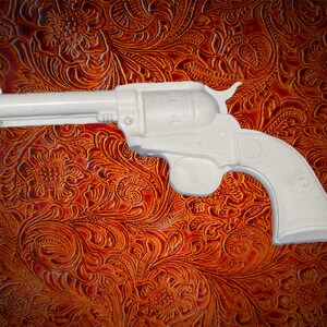 May include: A white plastic toy revolver with a black barrel. The toy gun is on a brown patterned background.