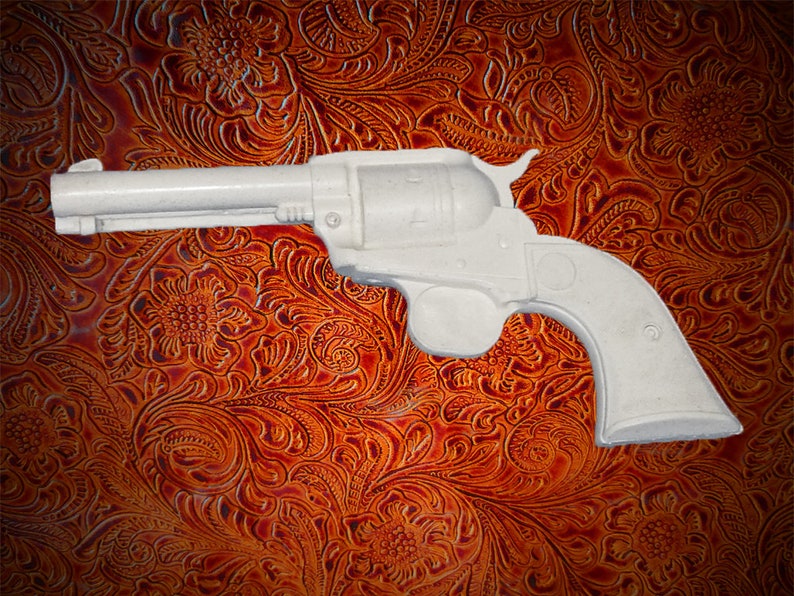 May include: A white plastic toy revolver with a black barrel. The toy gun is on a brown patterned background.