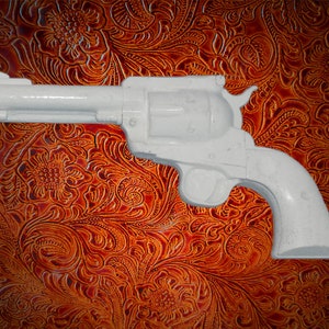 May include: A white plastic toy revolver, a replica of a classic six-shooter, is shown against a brown leather background with a floral pattern.