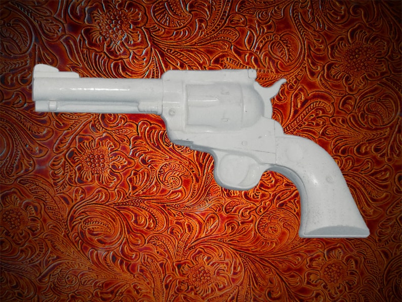 May include: A white plastic toy revolver, a replica of a classic six-shooter, is shown against a brown leather background with a floral pattern.