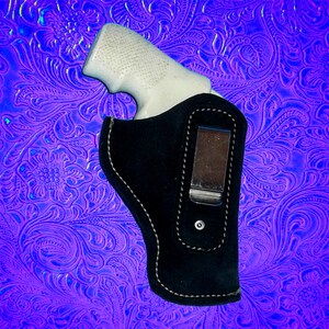 May include: A black leather holster with a clip for a gun. The holster is on a purple and blue patterned background.