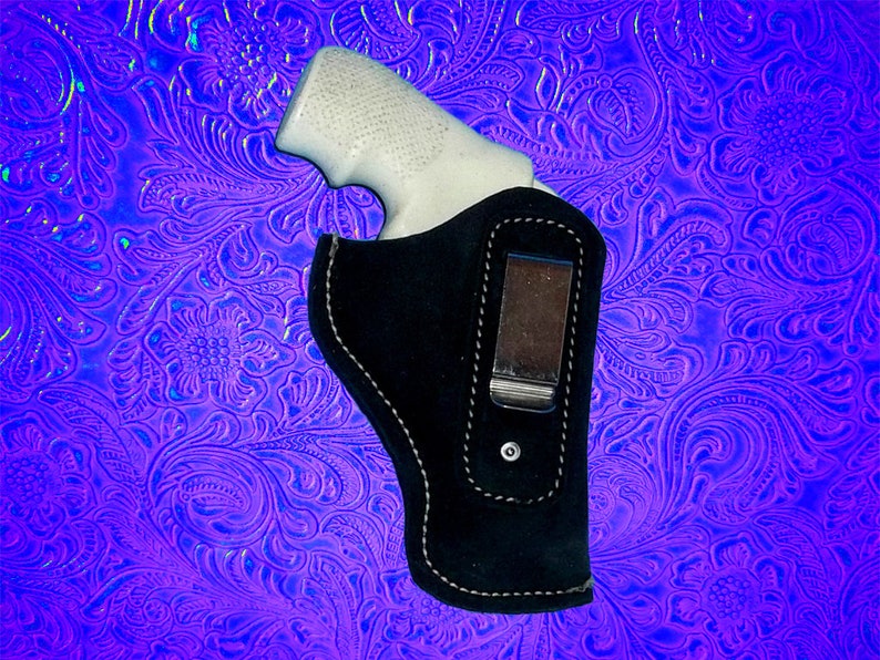 May include: A black leather holster with a clip for a gun. The holster is on a purple and blue patterned background.